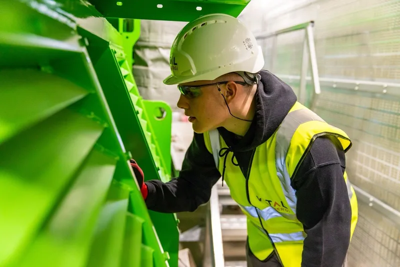 A worker in a hard hat and high-visibility vest examining green industrial equipment.