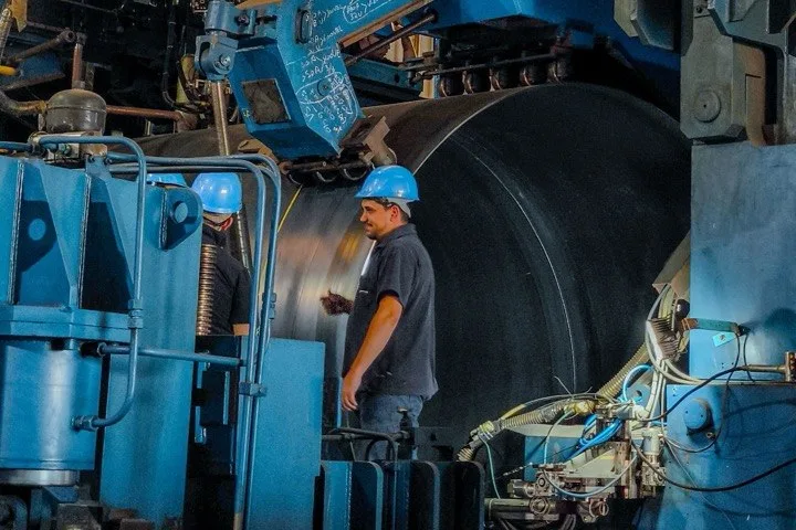 Two workers in hard hats beside large blue machinery in an industrial plant.